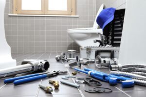 Plumber tools on the floor of a bathroom near an open toilet.